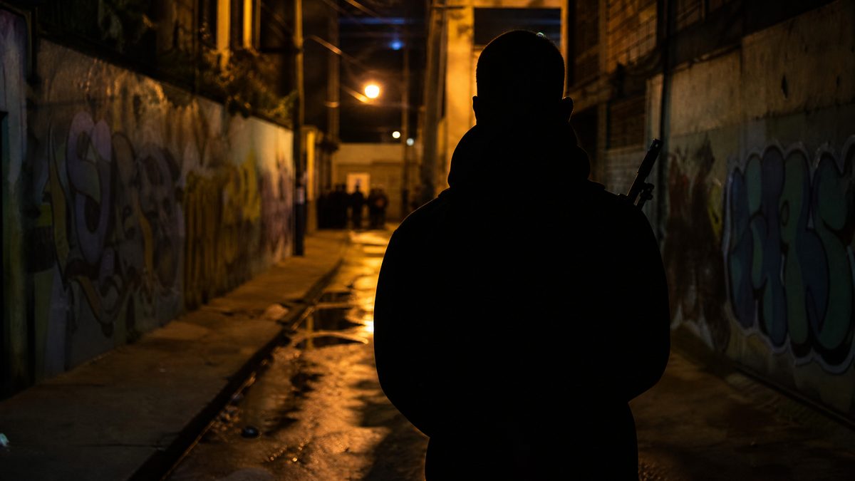 Silueta de figura armada en callejón urbano latinoamericano