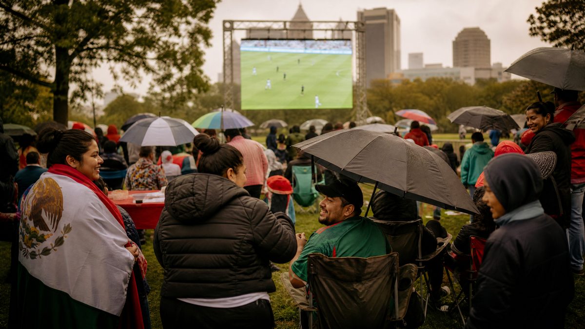 Comunidad latina en Columbus viendo fútbol bajo la lluvia con paraguas